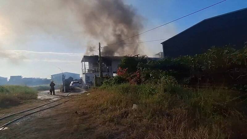 胜兴薪炭号承租的永成路仓库午后突起火，铁皮建物窜出浓烟，消防员布线灌救控制火势，现场无人受伤受困。（民众提供）